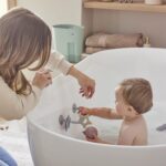 Shnuggle stick n play on side of big bath with toddler playing 3 square
